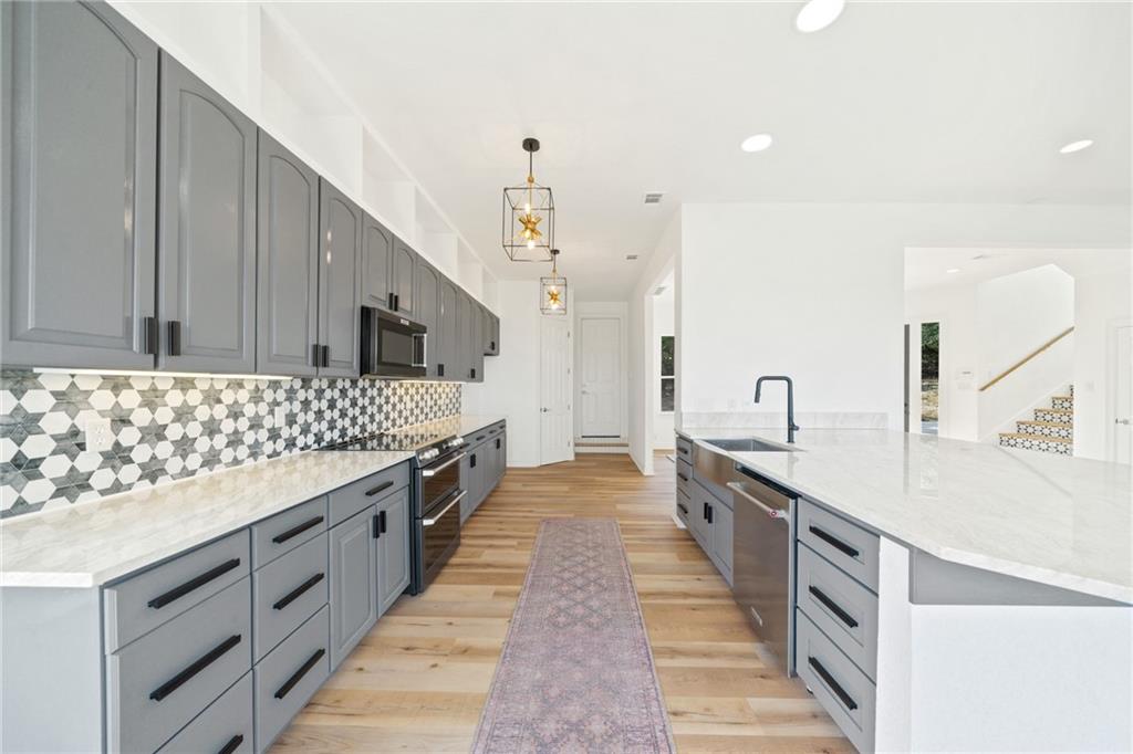 13301 Lone Rider Trail Bee Cave, TX 78738 - Photo 5 of 21 The kitchen features light-colored hardwood flooring, grey cabinetry with black hardware, a tiled backsplash, and stainless steel appliances