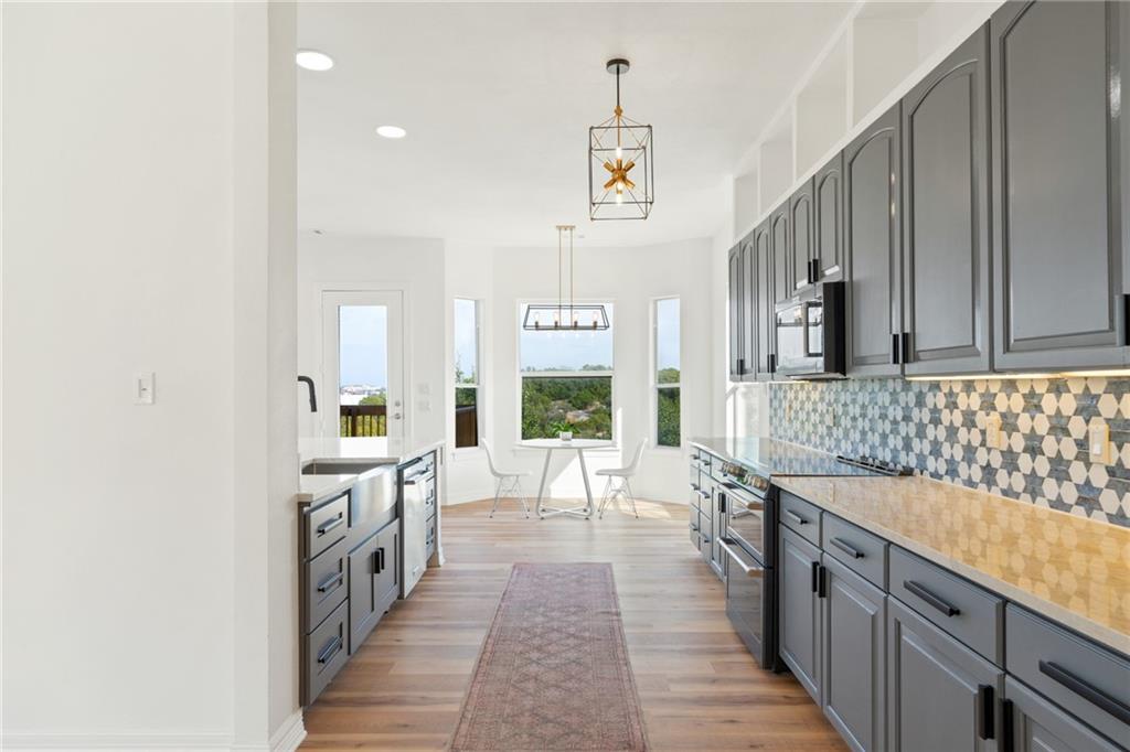 13301 Lone Rider Trail Bee Cave, TX 78738 - Photo 6 of 21 The kitchen features gray cabinetry with black hardware, light-colored countertops, and a patterned tile backsplash