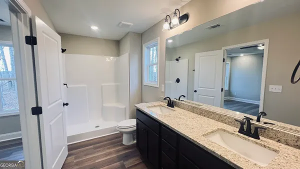 a bathroom with a granite countertop double vanity sink a mirror and a shower