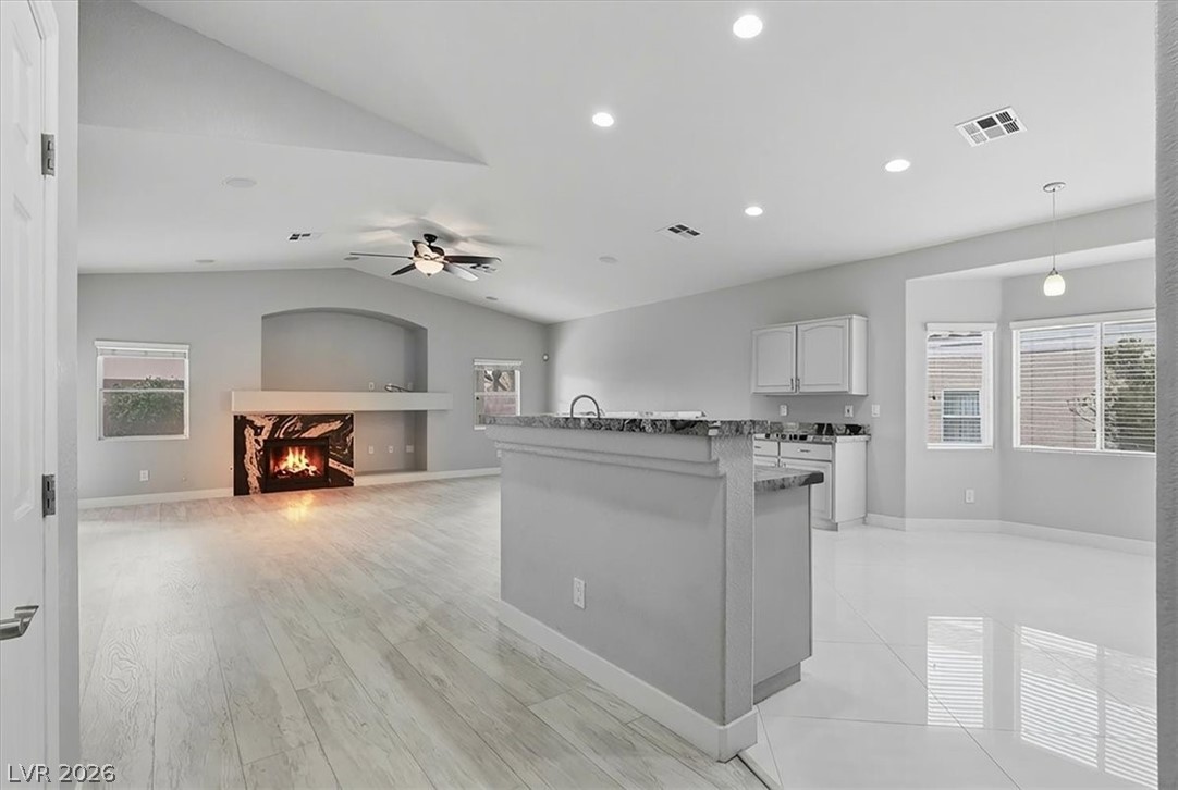 2413 Gold Camp Street Henderson, NV 89002 - Photo 6 of 66 Great room / Kitchen featuring healthy amount of natural light, vaulted ceiling, a lit fireplace, white cabinetry, and ceiling fan.