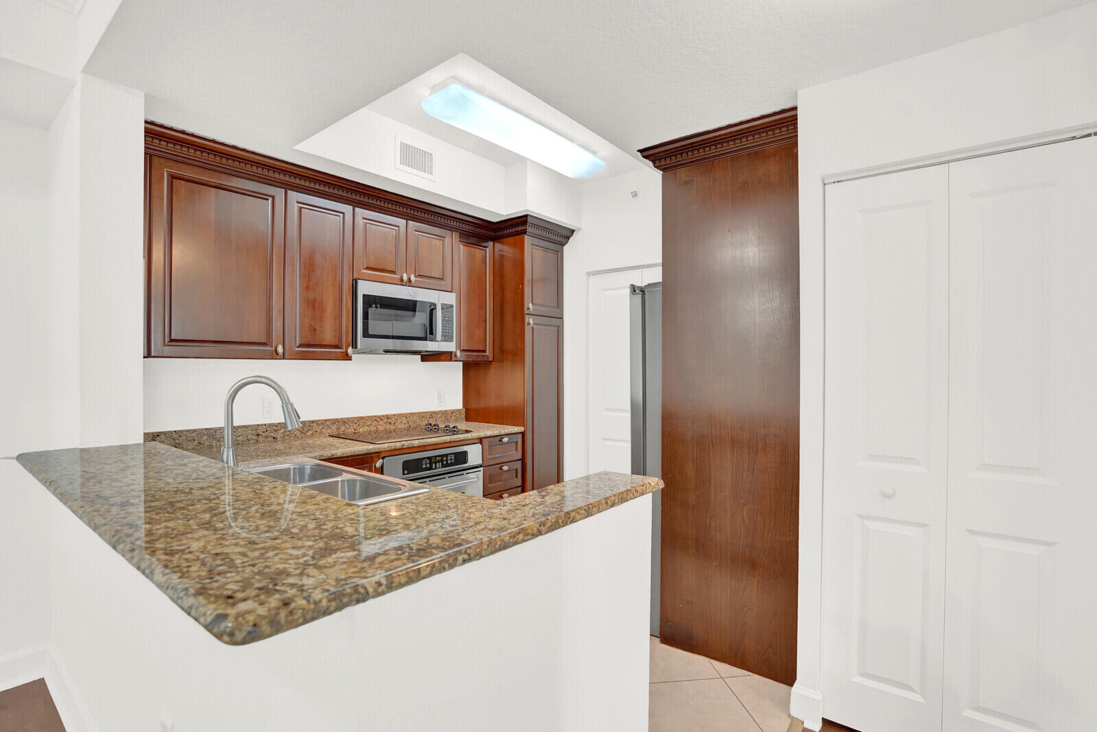 1690 Renaissance Commons Boulevard, Unit 1121 Boynton Beach, FL 33426 - Photo 7 of 32 a kitchen with granite countertop a sink refrigerator and microwave