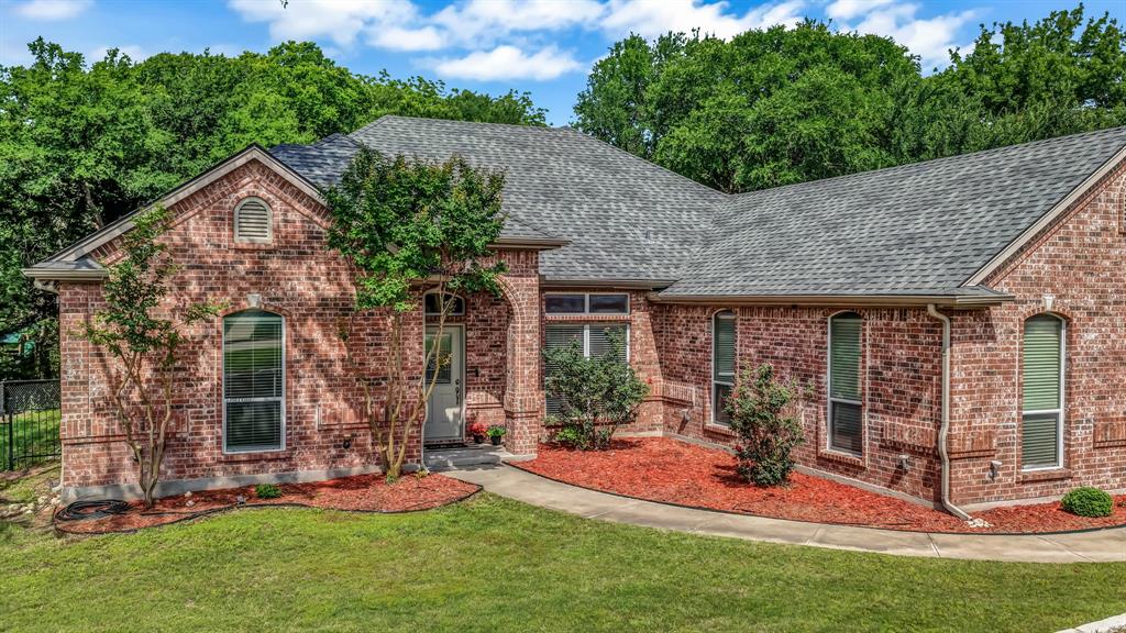 203 Mockingbird Lane Aledo, TX 76008 - Photo 4 of 37 Brick exterior with a gray shingle roof, arched entryway, manicured landscaping with red mulch, and a concrete walkway
