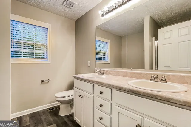 a bathroom with a granite countertop toilet a sink a mirror and a window