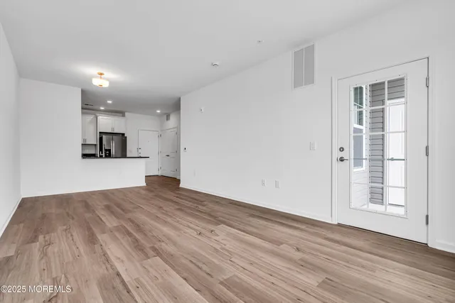 an empty room with wooden floor and a kitchen