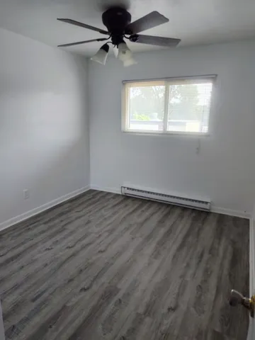an empty room with wooden floor fan and windows