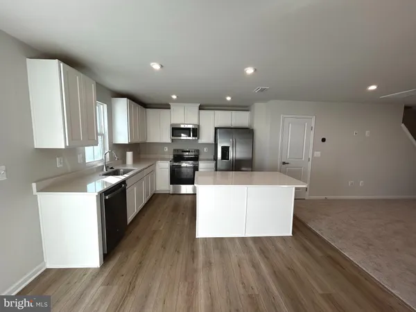 a large kitchen with a large counter top a sink stainless steel appliances and cabinets