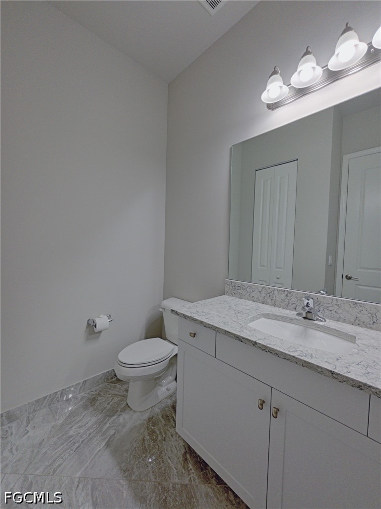4129 Amelia Way Naples, FL 34119 - Photo 14 of 23 a bathroom with a granite countertop sink a toilet and a mirror