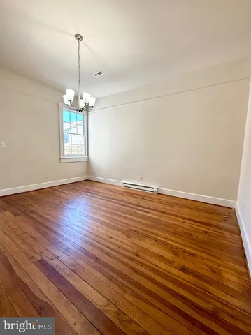 a view of an empty room with wooden floor fridge and a window