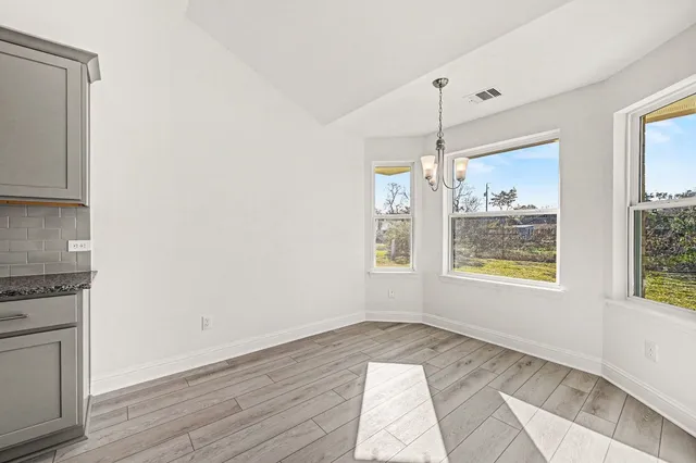 a view of an empty room with wooden floor and windows