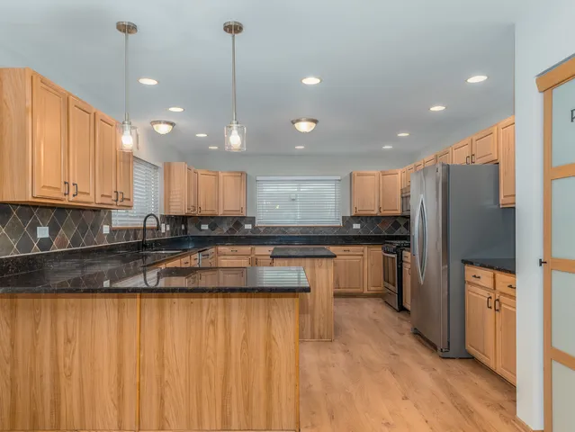 a kitchen with stainless steel appliances granite countertop a refrigerator a sink dishwasher a stove and white countertops with wooden floor