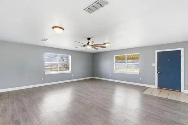 an empty room with wooden floor chandelier fan and windows