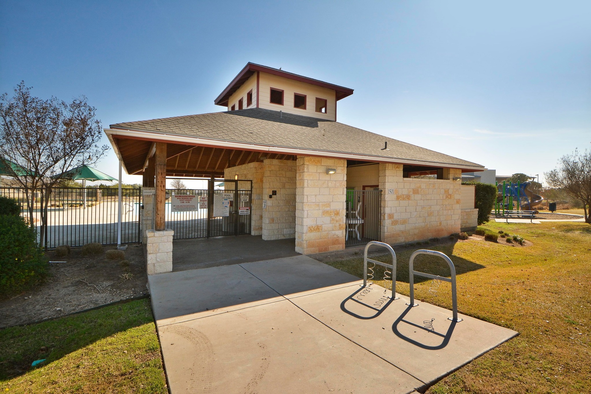 1818 Lost Maples Loop Cedar Park, TX 78613 - Photo 32 of 38 An inviting stone and wood-accented community building stands beside a gated pool area, with a playground visible in the background.