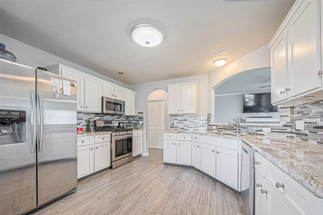 a kitchen with stainless steel appliances granite countertop a stove top oven a sink dishwasher a refrigerator and a refrigerator with wooden floor