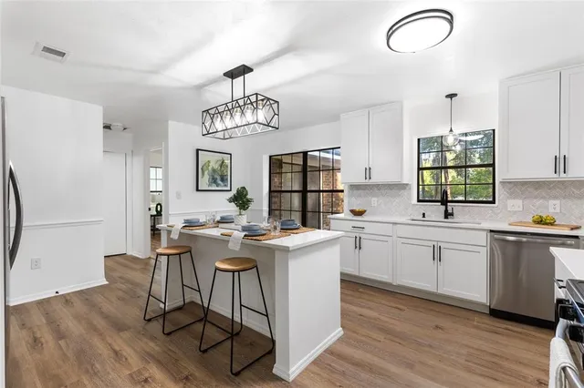 a kitchen with stainless steel appliances granite countertop a stove top oven a sink dishwasher and white cabinets with wooden floor