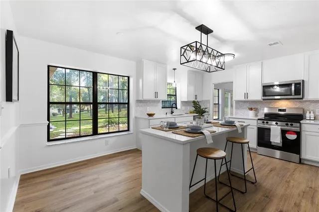 a kitchen with stainless steel appliances granite countertop a stove top oven a sink dishwasher a dining table and chairs with wooden floor