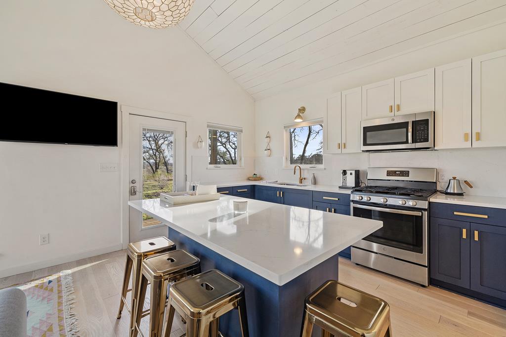 444 Klein Road Stonewall, TX 78671 - Photo 33 of 55 a kitchen with stainless steel appliances a stove a sink a microwave a refrigerator a stove and white cabinets with wooden floor