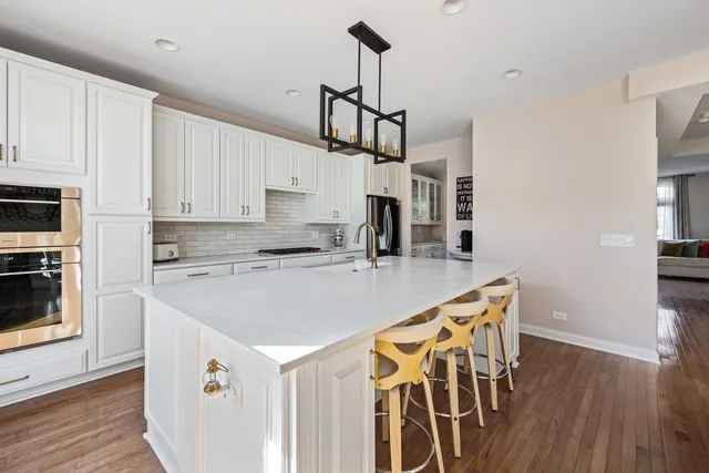 a kitchen with stainless steel appliances granite countertop a kitchen island a stove a sink a refrigerator white cabinets and wooden floor