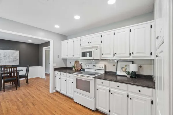 a white kitchen with granite countertop a sink a stove a dining table and chairs with wooden floor