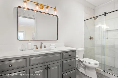 a bathroom with a toilet a sink a glass door a shower and mirror