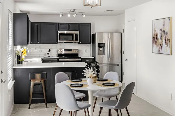a kitchen with stainless steel appliances a dining table chairs refrigerator and microwave