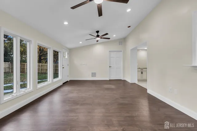 a view of an empty room and a kitchen with wooden floor