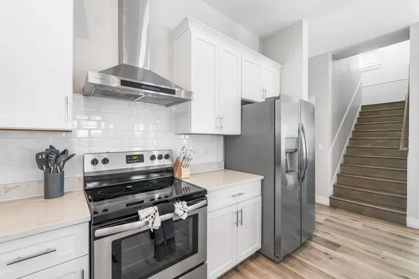 a kitchen with stainless steel appliances granite countertop a refrigerator a sink dishwasher a stove and white cabinets with wooden floor