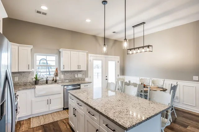 a kitchen with stainless steel appliances kitchen island granite countertop a refrigerator a stove a sink a dining table and chairs with wooden floor