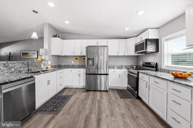 a kitchen with stainless steel appliances granite countertop a stove a sink dishwasher a refrigerator and white cabinets with wooden floor