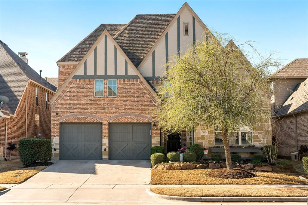 Tudor house featuring an attached garage, stucco siding, concrete driveway, stone siding, and brick siding