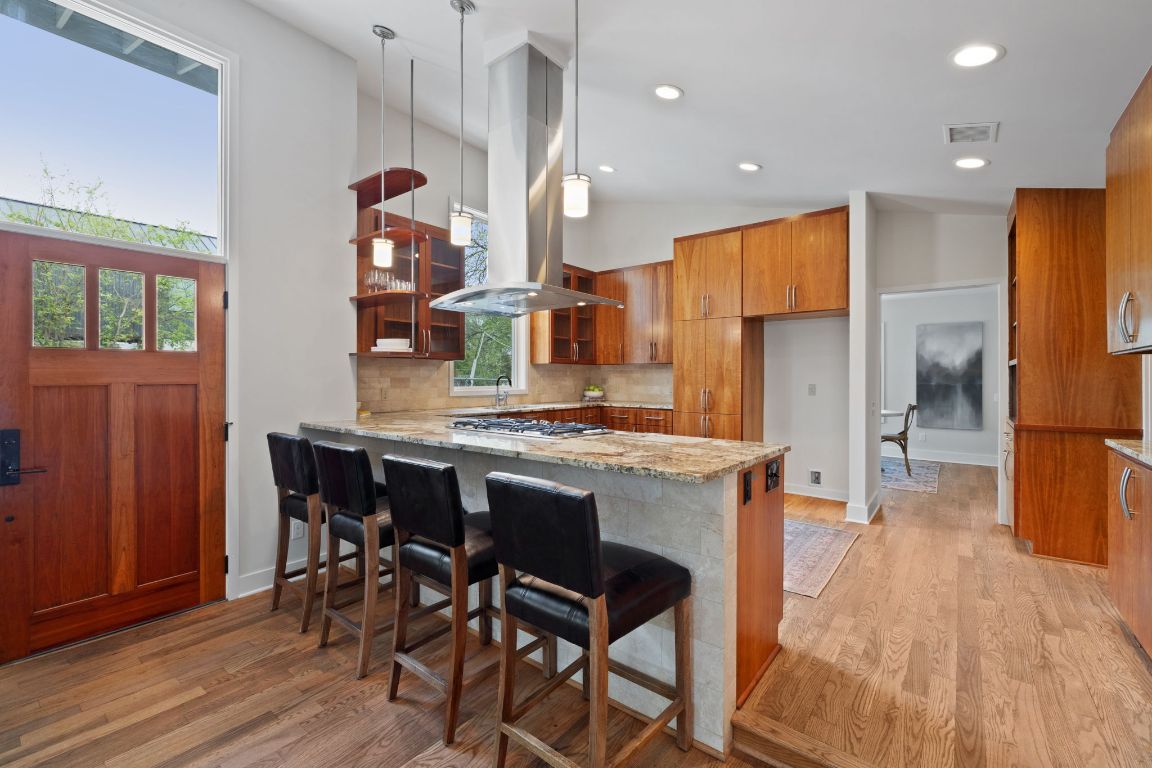 2300 South 3rd Street Austin, TX 78704 - Photo 11 of 39 Kitchen featuring light stone counters, a peninsula, brown cabinetry, island exhaust hood, and light wood-style floors