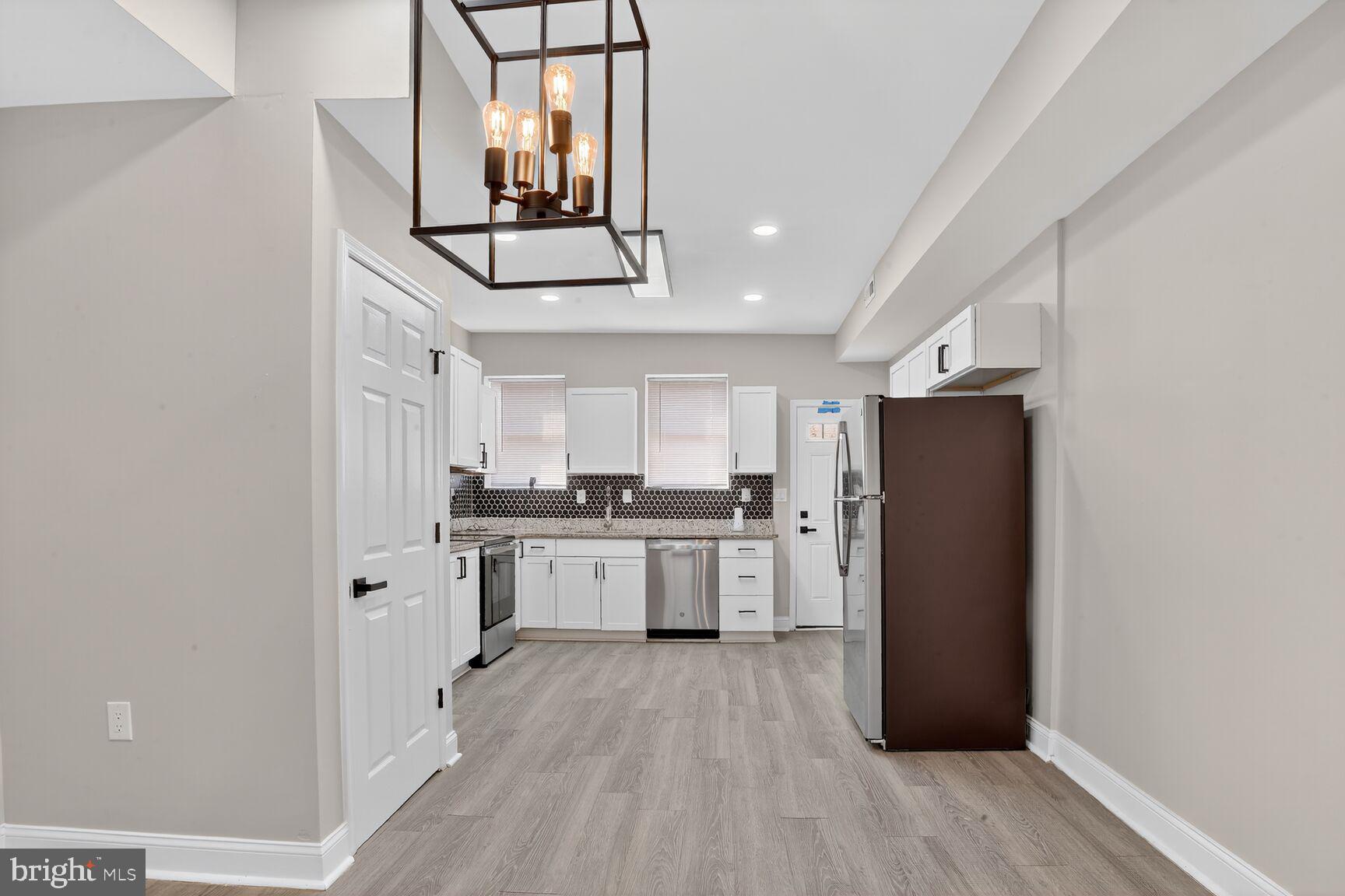1106 South Carey Street Baltimore, MD 21223 - Photo 7 of 24 a kitchen with refrigerator a microwave a stove and white cabinets with wooden floor