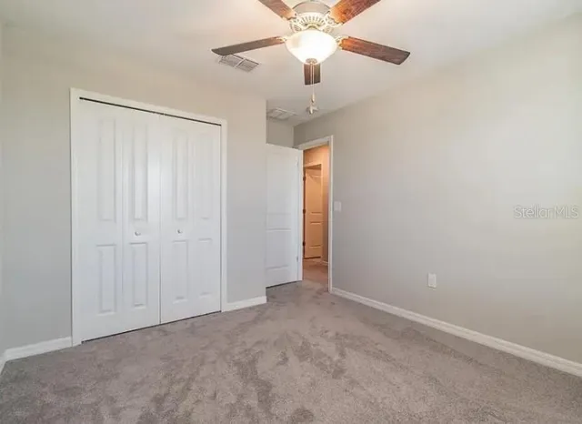 an empty room with a chandelier fan and closet area
