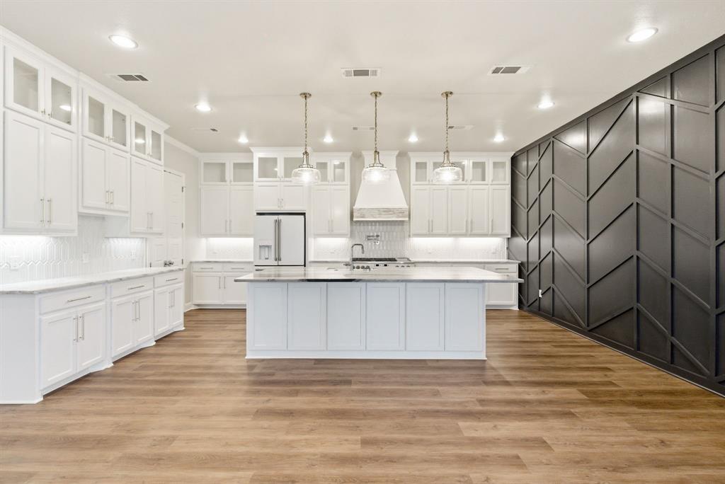 4600 Old Brock Road Weatherford, TX 76087 - Photo 11 of 37 Contemporary kitchen featuring an expansive center island with pendant lighting, stone countertops, white cabinetry with glass-front accents, stainless steel appliances, and wood-finish flooring