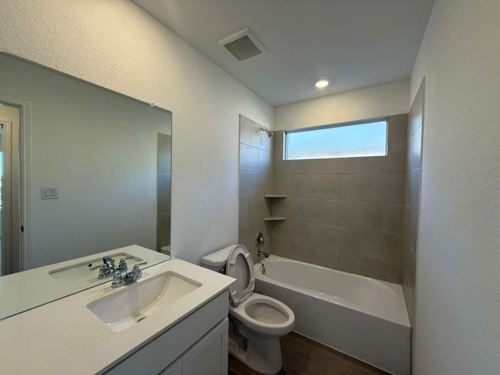 545 Sormonne Loop Kyle, TX 78640 - Photo 30 of 39 Bathroom featuring vanity, shower combination, a textured wall, and dark wood-type flooring