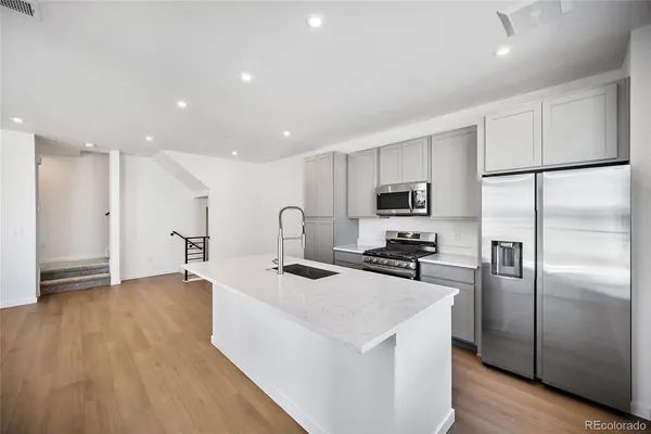a kitchen with stainless steel appliances granite countertop a refrigerator a oven a sink a stove and white cabinets with wooden floor