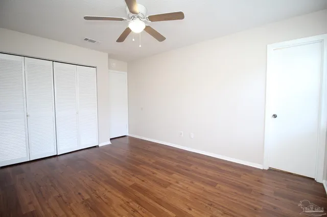 an empty room with wooden floor fan and windows