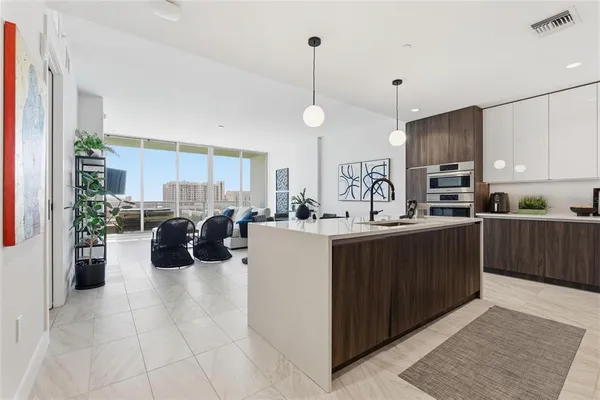 a kitchen with stainless steel appliances kitchen island granite countertop a refrigerator a sink dishwasher and a view of living room with wooden floor