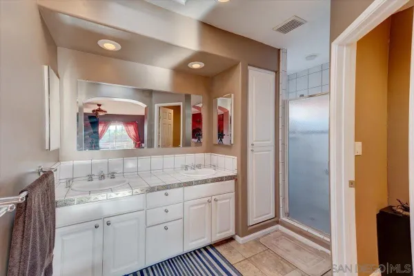 a bathroom with a granite countertop double vanity sink a mirror and a shower