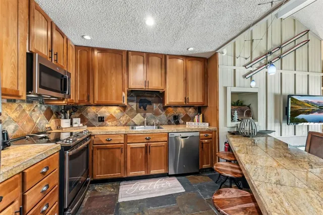 a kitchen with stainless steel appliances granite countertop wooden cabinets a sink dishwasher a stove and a refrigerator with wooden floor