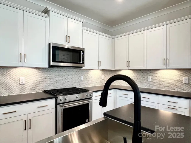 a kitchen with stainless steel appliances granite countertop a stove a microwave a sink and cabinets with wooden floor