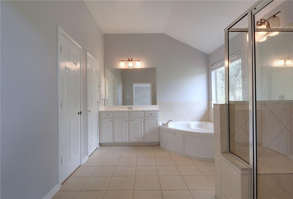 13017 Titus Court Austin, TX 78732 - Photo 19 of 26 Full bath with vaulted ceiling, a bath, vanity, light tile patterned flooring, and a stall shower
