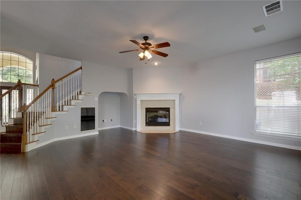13017 Titus Court Austin, TX 78732 - Photo 2 of 26 Unfurnished living room featuring a fireplace with flush hearth, stairs, dark wood-style floors, ceiling fan, and arched walkways