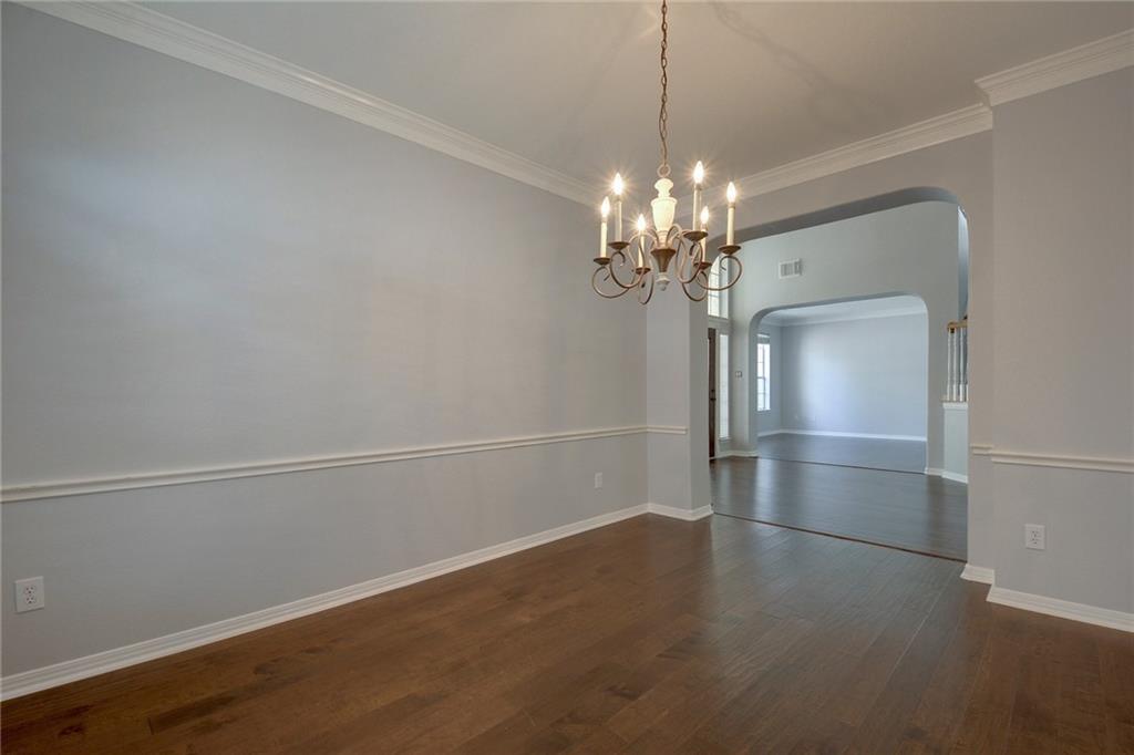 13017 Titus Court Austin, TX 78732 - Photo 9 of 26 Unfurnished room featuring arched walkways, dark wood-style flooring, crown molding, and a chandelier