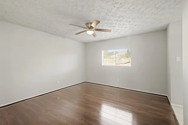 an empty room with wooden floor ceiling fan and windows