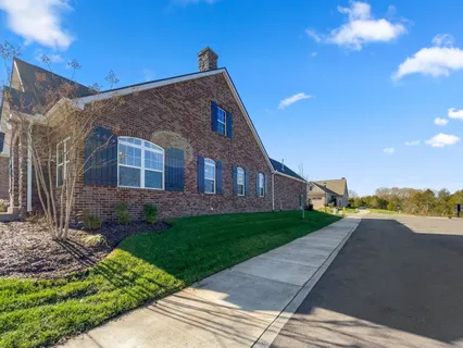 a view of a brick house next to a yard with big trees