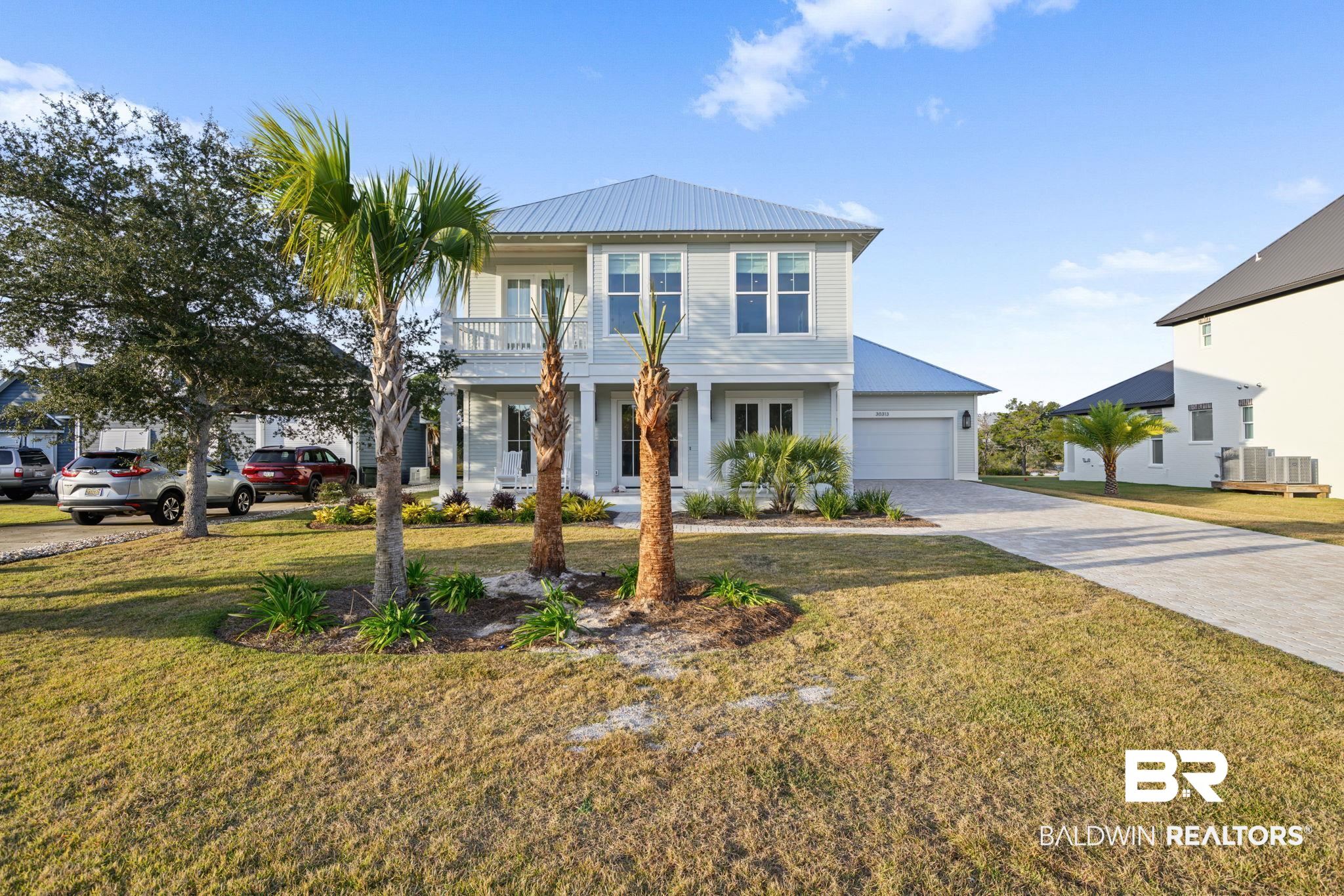 30313 River Road Orange Beach, AL 36561 - Photo 5 of 50 View of front of home featuring decorative driveway, a front lawn, a metal roof, covered porch, and a balcony