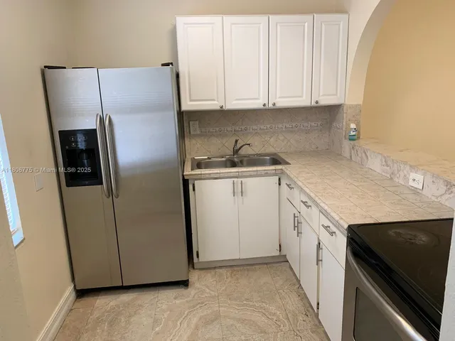 a kitchen with stainless steel appliances granite countertop a refrigerator a sink and white cabinets