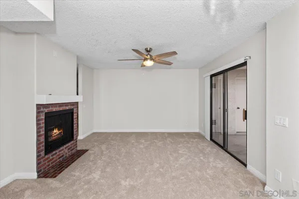 a view of an empty room with chandelier fan and fire place
