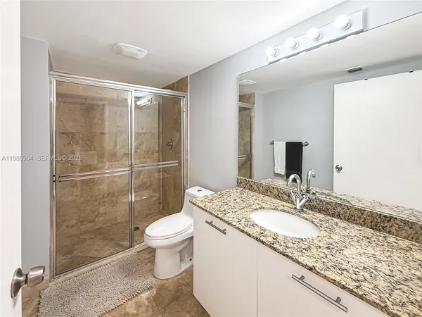 a bathroom with a granite countertop sink a toilet a mirror and shower