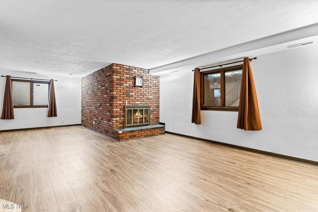 3863 Sourek Rd Extension Akron, OH 44333 - Photo 18 of 42 Unfurnished living room featuring a textured ceiling, wood finished floors, a brick fireplace, and plenty of natural light